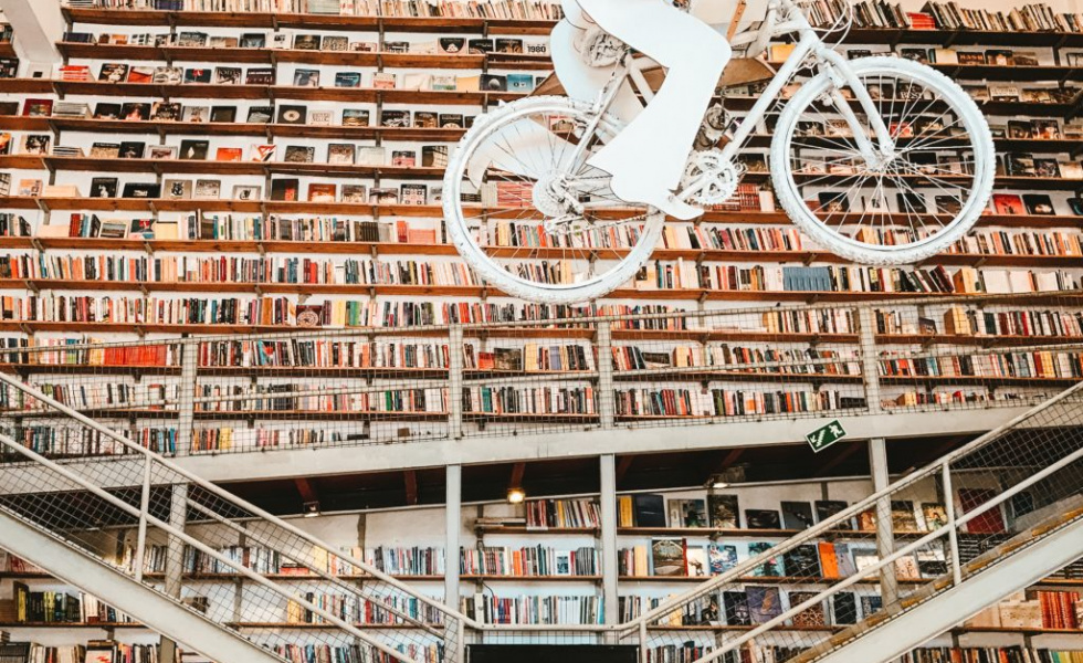 Inside of a library with a bicycle sculpture hanging from the cieling