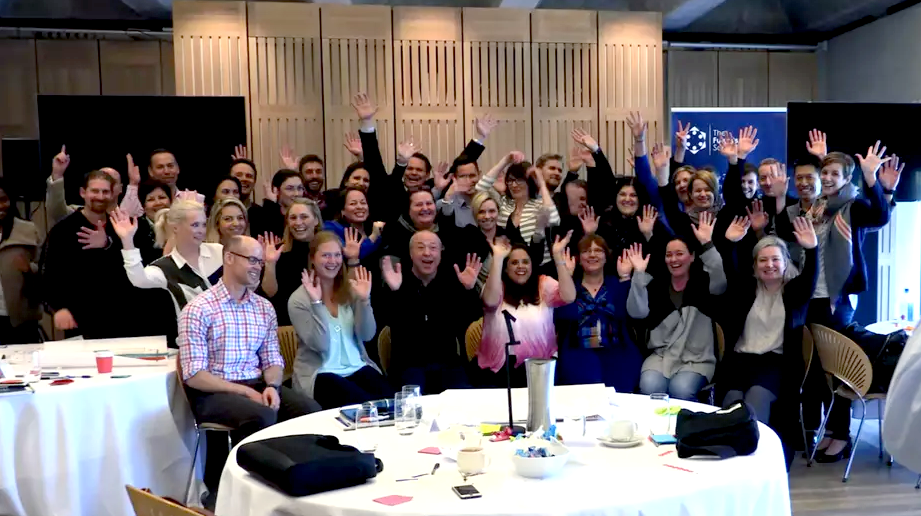 A large group of people smiling and waving hands for a picture